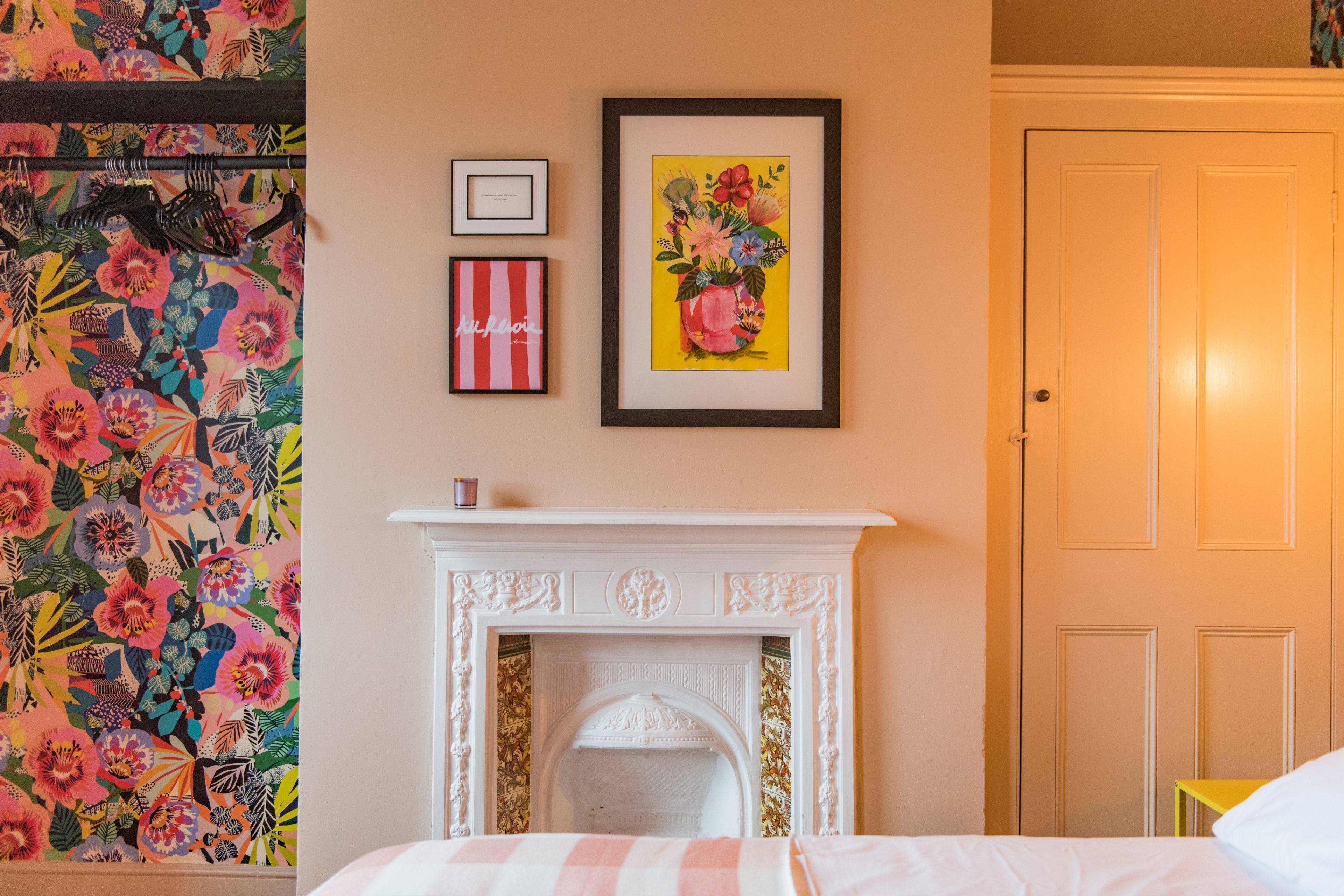 Ein Zimmer mit Bett, Kamin, Tür und blumigem Wandpapier.
