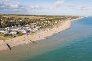 A coastal town with houses along the beach, a clear sky, and calm sea. - Pebble Beach Cottage (Kingsdown)
