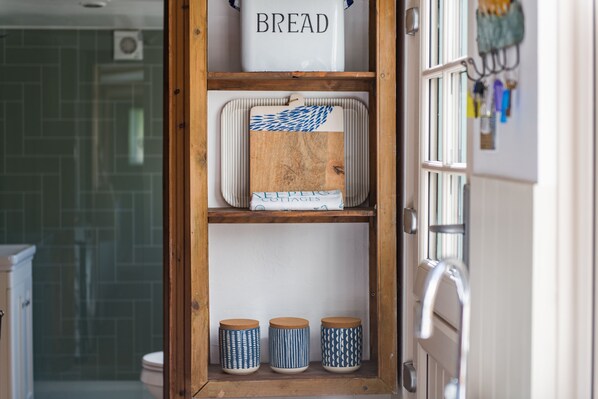 A kitchen with a wooden cabinet containing a bread container, a cutting board, and three patterned containers. - Pebble Beach Cottage (Kingsdown)