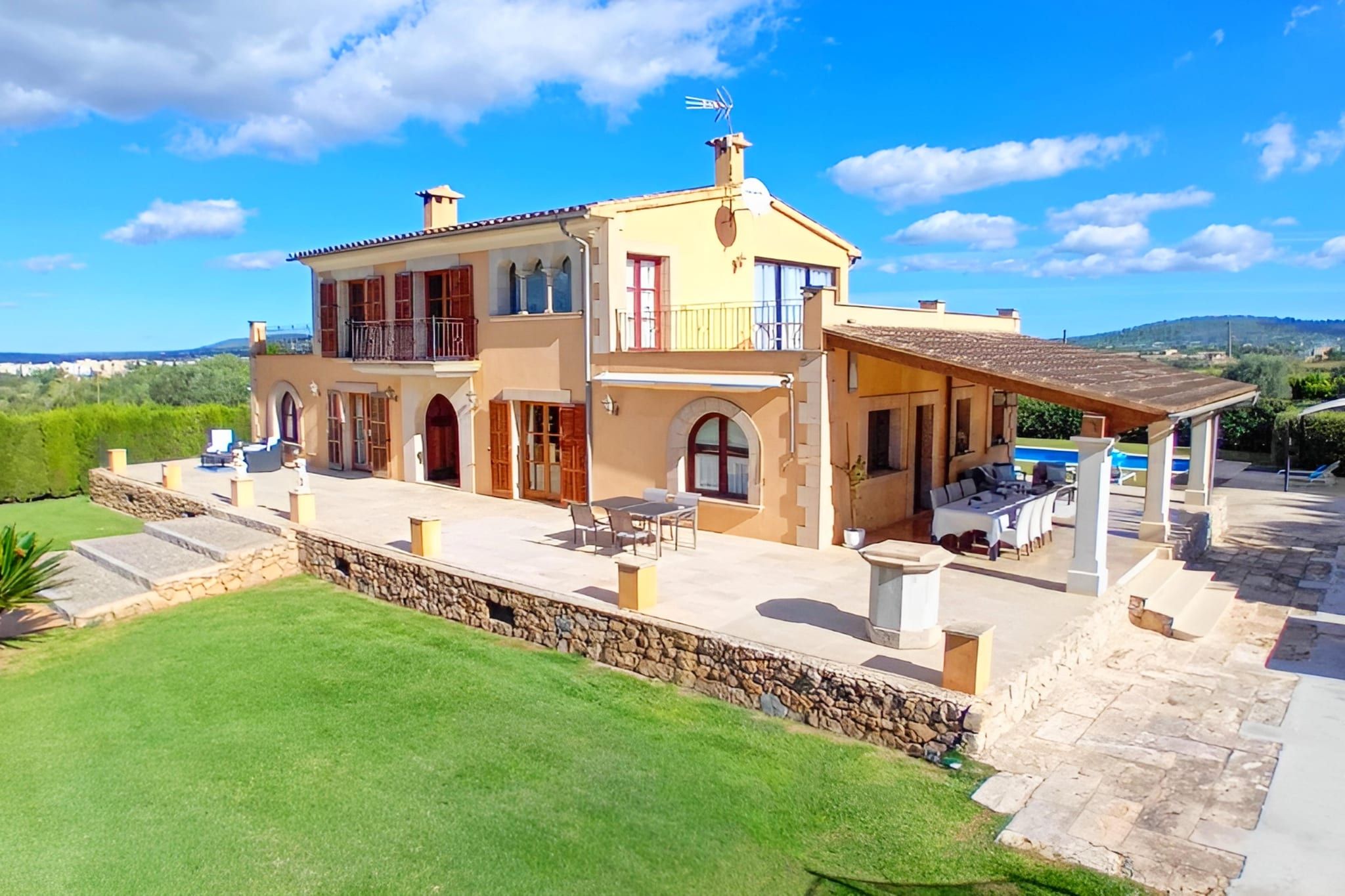 A two-story house with a balcony, a swimming pool, and a stone retaining wall.