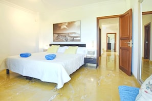 Een hotelkamer met een bed, een nachtkastje, een schilderij en een deur naar een andere kamer.
