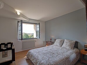 A bedroom with a bed, a nightstand, a window with curtains, a radiator, and a view of the outdoors. - Country cottage with terrace - 5 guests (Marcenod)