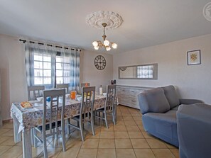 A dining area with a table set for four, a chandelier, a clock, and a sofa. - Country cottage with terrace - 5 guests (Marcenod)
