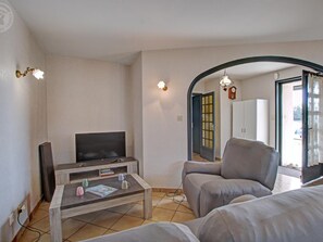 A living room with a flat-screen TV, a coffee table with books and mugs, a grey sofa, and a door leading to another room. - Country cottage with terrace - 5 guests (Marcenod)