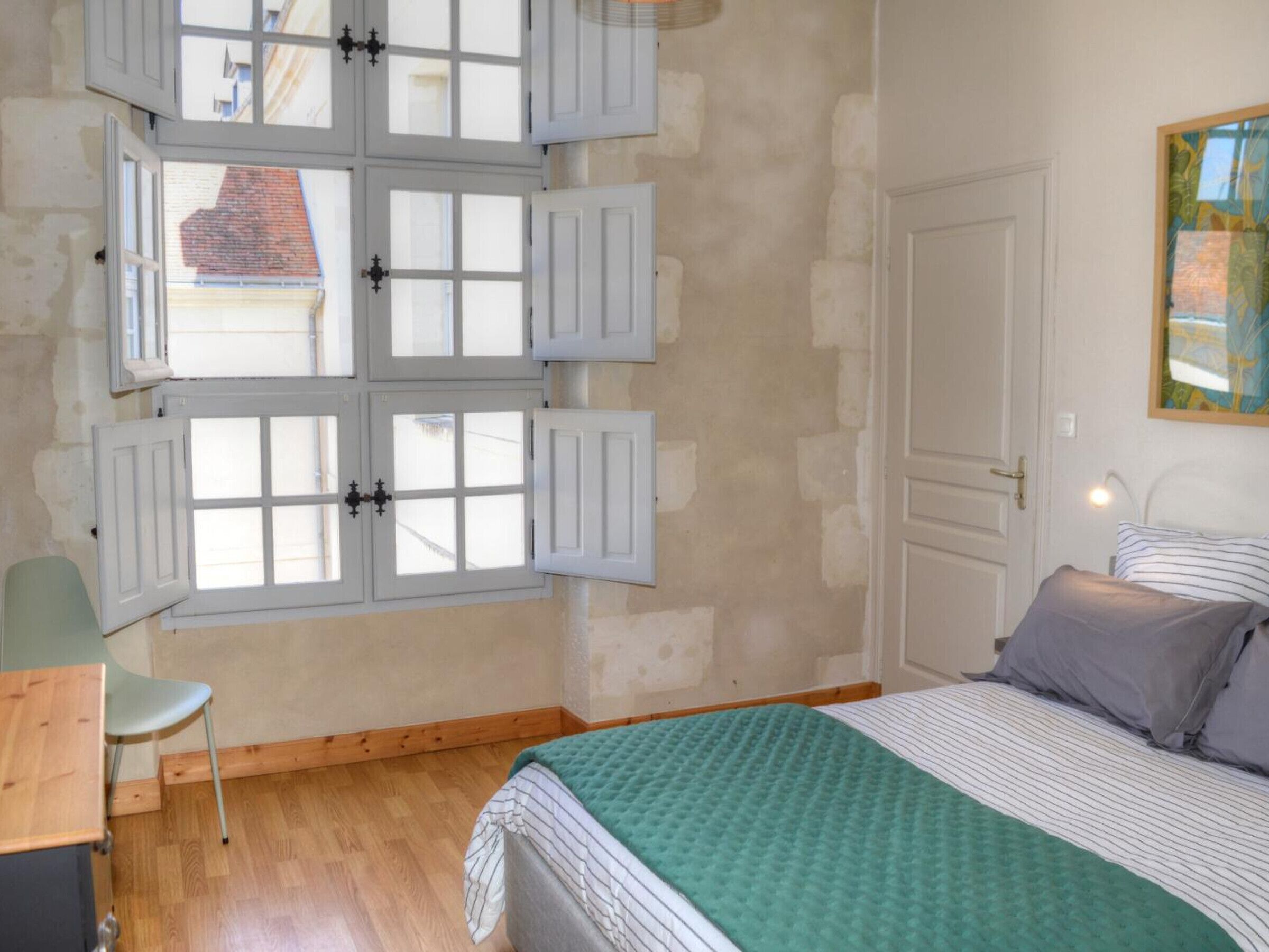 A bedroom with a bed, a chair, a desk, and a window with shutters.