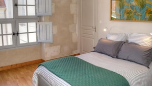Een slaapkamer met een bed, een deur en een raam met luiken.