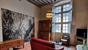 Een woonkamer met een rode bank, een houten kast, een schilderij en een groot raam met luiken.