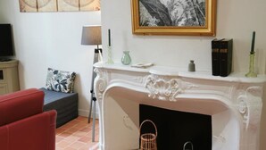 Een woonkamer met een open haard, een rode bank, een lamp en een schilderij aan de muur.