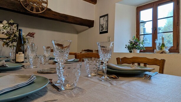 Mesa de jantar posta com copos de cristal, pratos e uma garrafa de vinho.