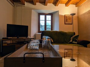 Un salon avec une télévision, une table en verre sur laquelle sont posés des verres à vin, un banc en bois et une fenêtre donnant sur un paysage.