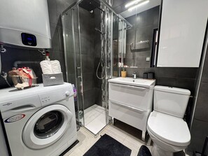 Un baño moderno con cabina de ducha de vidrio, lavadora integrada, lavamanos y retrete.