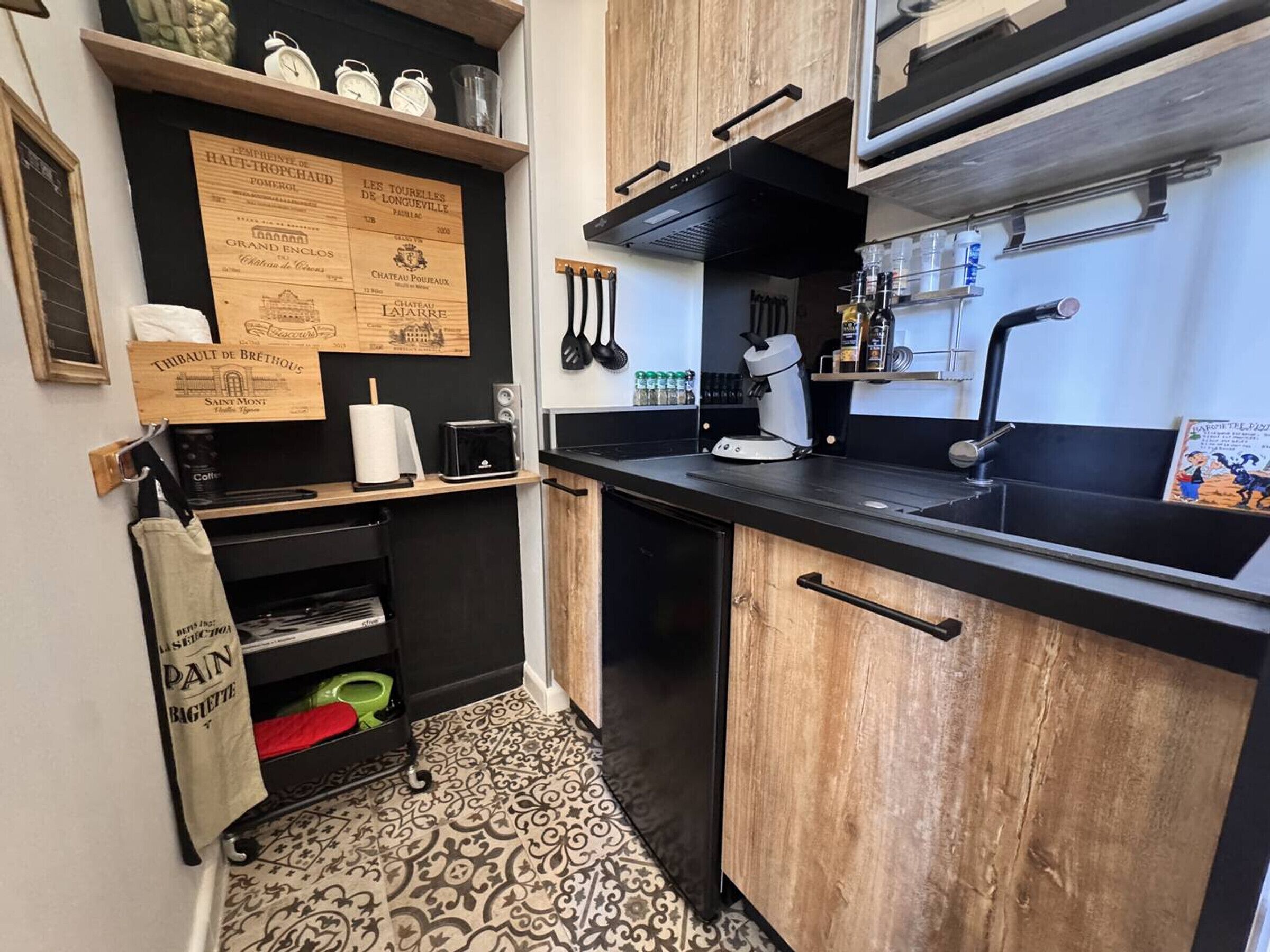 Uma cozinha compacta com bancada preta, armários de madeira, cafeteira e pia.