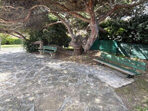 A stone-paved park area with two green benches under a large tree. - Renovated studio, parking - 4 guests (Six-Fours-les-Plages)