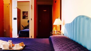 Une chambre d’hôtel avec un lit, un plateau contenant des articles pour le petit-déjeuner, une table de chevet avec une lampe et une porte donnant sur une autre pièce.