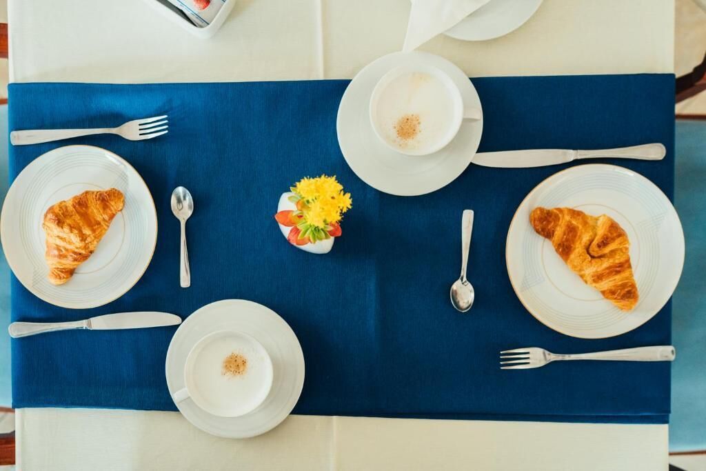 A table set with croissants, coffee cups, and a small flower arrangement.