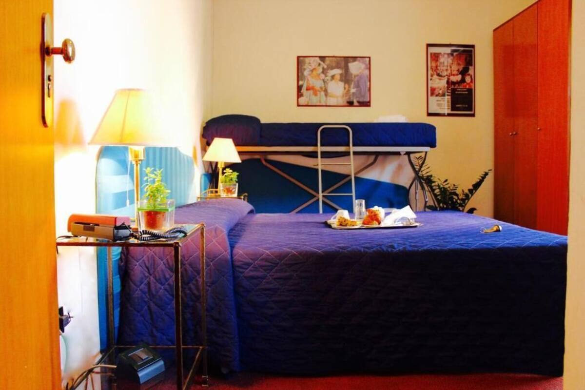 Una habitación con una cama individual superpuesta, un escritorio con lámpara, una planta pequeña y un cartel en la pared.