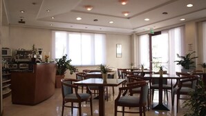 Un hall d’hôtel doté de nombreuses tables et chaises, d’un comptoir de réception et de grandes fenêtres laissant entrer la lumière naturelle.
