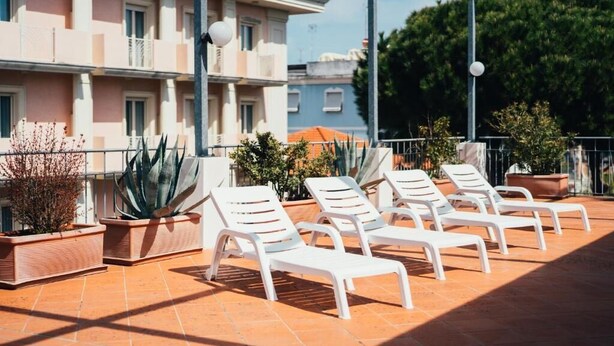 Une terrasse sur le toit, avec des chaises longues blanches, des plantes en pot et un bâtiment en arrière-plan.