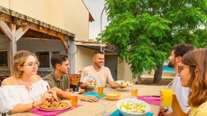 Un gruppo di persone cena all'aperto a un tavolo di legno, con cibo e bevande.