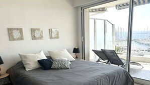 A bedroom with a large bed, a nightstand, a lamp, and a view of a marina through a sliding glass door. - Studio cabin sea view - 4 guests (Saint-Raphaël)