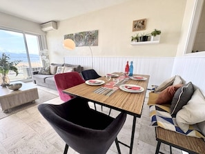 Ein Essbereich mit Tisch für vier Personen, einer Couch, einem Sessel und Blick ins Freie.
