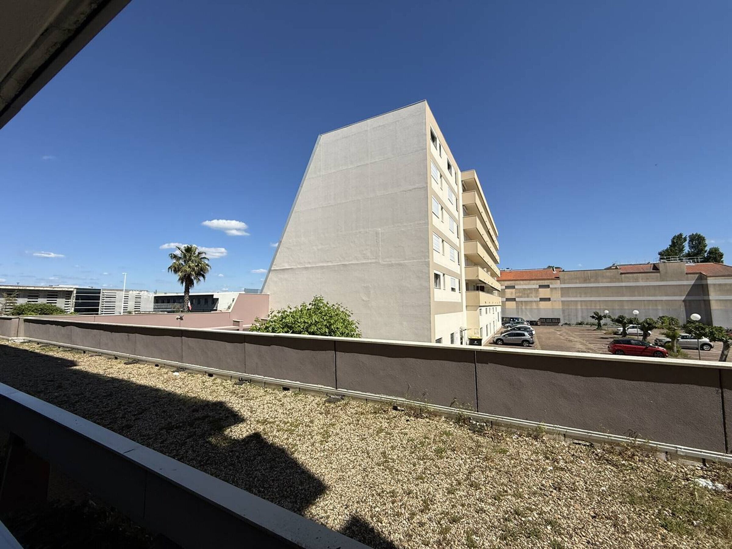 Un bâtiment doté d’un toit plat, un parking où sont garées plusieurs voitures et un ciel bleu dégagé.