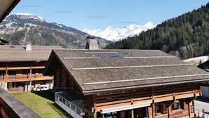 Un chalet en bois avec un toit en pente, des panneaux solaires et une vue sur des montagnes enneigées.