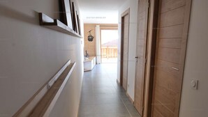 Un couloir avec une porte en bois, un mur blanc et un sol carrelé.