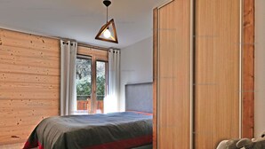 Une chambre à coucher comprenant un lit, une armoire en bois, une chaise et un luminaire suspendu.