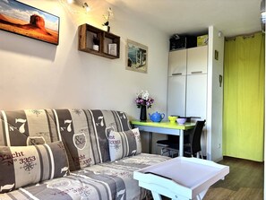Ein gemütlicher Wohnraum mit einer Couch, einem kleinen Esstisch, einem Schrank und einem Bild an der Wand.