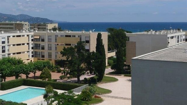 Edifício residencial com piscina, rodeado por vegetação e vista clara para o mar.