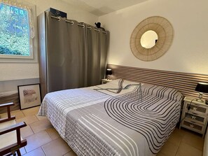 A bedroom with a bed, a bedside table, a lamp, a mirror, a curtain, and a framed picture on the wall. - Apartment with AC and parking - 4 guests (Gruissan)