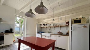 Eine Küche mit einem roten Tisch, weißen Schränken, einem Kühlschrank von Brandt, hängenden Pendelleuchten und einem gefliesten Boden.