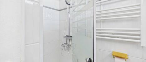 Una ducha con cabezal de ducha manual, puerta de cristal, toallero y un inodoro.