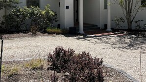 Un edificio moderno con un acceso cubierto, un camino de grava y un pequeño jardín.