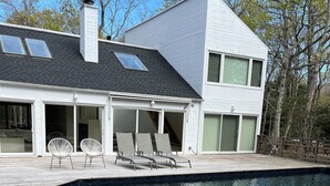 Una casa moderna con piscina, un patio cubierto con sillones de descanso y un ventanal grande.