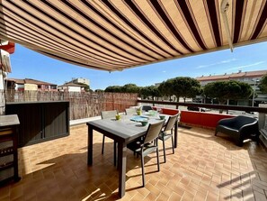 Eine Terrasse im Freien mit Tisch und Stühlen, einem Holzzaun und Blick auf Gebäude und Bäume.