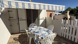 Um pátio com uma mesa posta para dois, cadeiras brancas e um cercado branco.
