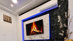 Un soggiorno moderno con una televisione a schermo piatto, due poltrone gialle, un tavolino rotondo e un camino.