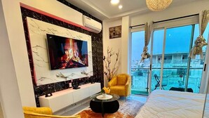 Una camera da letto moderna con televisore a parete, un letto, un divano e vista sulla città attraverso ampie finestre.