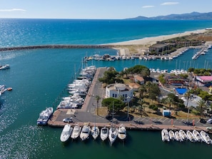 Ein Yachthafen mit vertäuten Booten, ein Strand im Hintergrund und ein kleines Gebäude mit rotem Dach.
