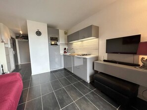 Eine kleine Küche mit grauen Schränken, einem eingebauten Backofen und einem flachbildfernseher an der Wand.