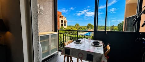 A balcony with a table set for dining, a cabinet, and a view of a building and greenery.