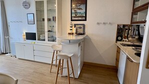 A compact kitchen with a dining area, a white cabinet with glass doors, a small island with stools, and a poster on the wall. - Studio with terrace port view - 4 guests (Gruissan)