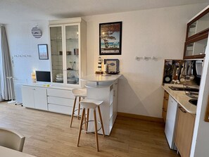 Eine kompakte Küche mit Essbereich, einem weißen Schrank mit Glastüren, einer kleinen Kochinsel mit Hockern und einem Poster an der Wand.