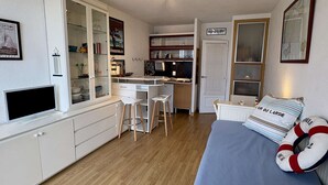 A compact room with a kitchenette, a bed with pillows, a television, and a wardrobe. - Studio with terrace port view - 4 guests (Gruissan)