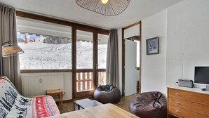 Una stanza con un tavolo di legno, un divano, un sacco di fagioli, una televisione e vista su un paesaggio innevato attraverso ampie finestre.