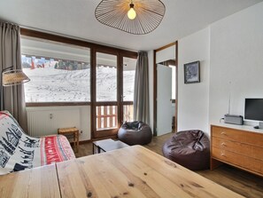 Ein Zimmer mit einem Holztisch, einer Couch, einem Sitzsack, einem Fernseher und Blick auf eine verschneite Landschaft durch große Fenster.