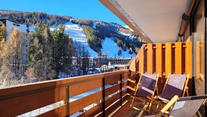 Een balkon met houten leuningen, twee loungestoelen en een uitzicht op een besneeuwd berglandschap.