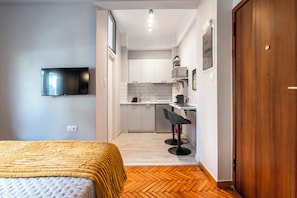 A compact room with a bed, a TV mounted on the wall, a kitchenette with a microwave, and a wooden door. - The Cozy Nest Ampelokipoi | 3’ walk from Metro (Athina)